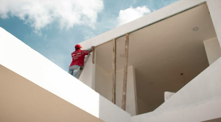 man in red jacket standing on white concrete building under blue and white cloudy sky during